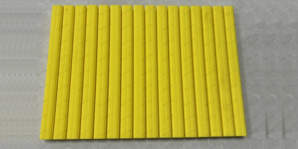 a collection of uniformly shaped, yellow objects arranged in rows on what appears to be a white surface. The items have a ribbed texture and are elongated with a cylindrical shape, reminiscent of drinking straws or perhaps some kind of plastic sticks used for crafting purposes. Their consistent size and color suggest they might be part of a larger set intended for a specific use or project.