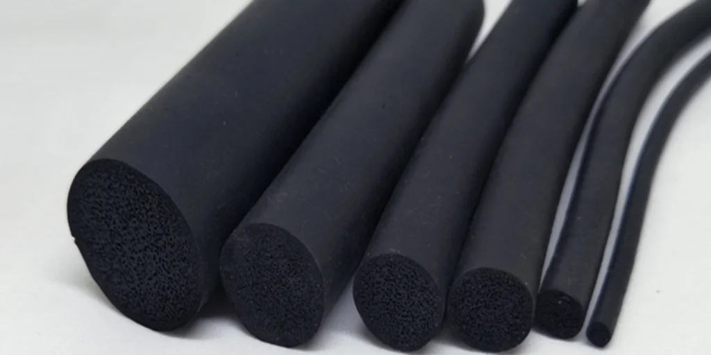 a collection of black cylindrical objects with varying diameters. They appear to be made from a porous material, likely rubber or plastic foam, given their texture and the way they are cut at different angles. The largest cylinder is placed on its side, while the others stand upright, showcasing their cross-sections which reveal the internal structure of the material. These objects could potentially serve as insulation materials due to their porous nature, which suggests good thermal properties.