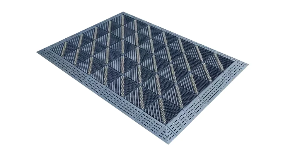 a modular entrance mat designed for high - traffic commercial or public spaces. The mat consists of interlocking sections, featuring a grid pattern with alternating dark and light - colored elements. The perimeter of the mat has a perforated design, likely to aid in water drainage and debris removal. Such mats are commonly used at building entrances to scrape dirt and moisture from footwear, helping to maintain clean and safe interior floors. The modular nature allows for easy replacement of individual sections if damaged and customization of size to fit different doorways.