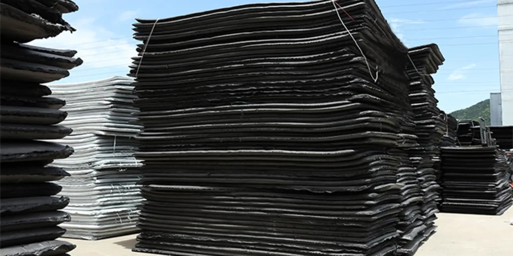 a large number of black and white objects stacked in piles. These objects appear to be made of rubber or plastic, with a smooth surface and a wavy edge design on one side. They are arranged neatly in rows, creating an orderly appearance. The background is a clear blue sky, suggesting that the photo was taken outdoors during the day.