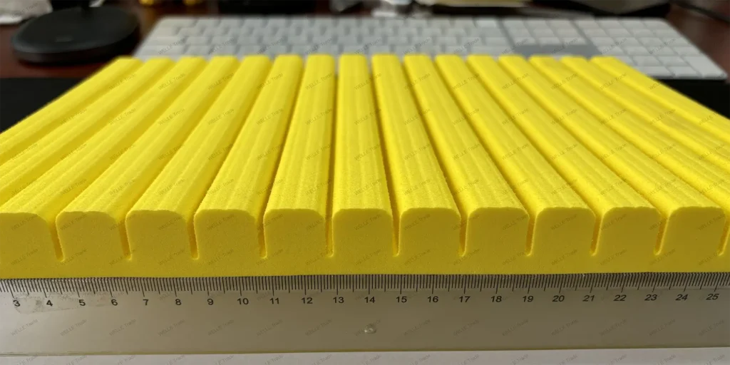 a collection of uniformly shaped, yellow objects arranged in rows on a flat surface. These objects appear to be cylindrical with a smooth texture and are placed next to a ruler for scale reference. The ruler indicates that each object is approximately 10 centimeters long. In the background, there’s an out-of-focus computer keyboard, suggesting this setup might be part of a workspace or laboratory environment. The uniformity and precision in the arrangement imply these items could be components used in some form of assembly or testing process.