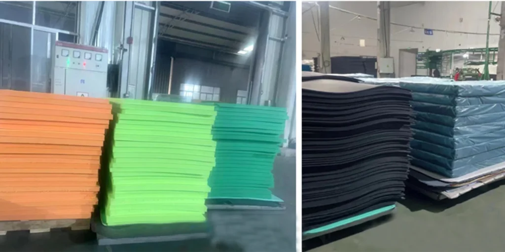 a warehouse or factory environment with various stacks of colored materials. On the left, there are neatly arranged piles of orange and green sheets placed on wooden pallets. In the background, we can see industrial equipment such as electrical panels and what appears to be machinery for material processing.On the right side of the image, there is another set of stacked materials in blue and black colors, also resting on pallets. The setting suggests an area where different types of raw materials or products are stored before further use or distribution.