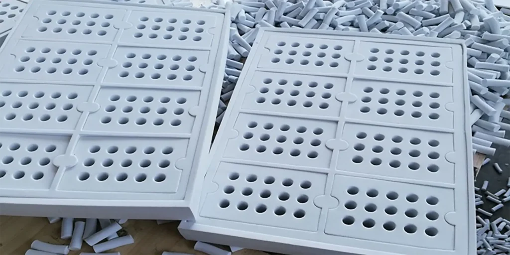 AlternativeText: Two white perforated foam panels with numerous circular holes, surrounded by cylindrical cut - out pieces. Caption: Perforated White Foam Panels with Circular Holes and Cylindrical Cut - Outs Description: The image shows two large white foam panels, each divided into sections filled with circular holes. Surrounding the panels are numerous small cylindrical pieces, likely cut - outs from the perforation process. The foam appears to be part of a manufacturing or crafting workflow, highlighting precise cutting. The wooden surface in the background adds a rustic contrast to the structured, industrial - looking foam pieces.