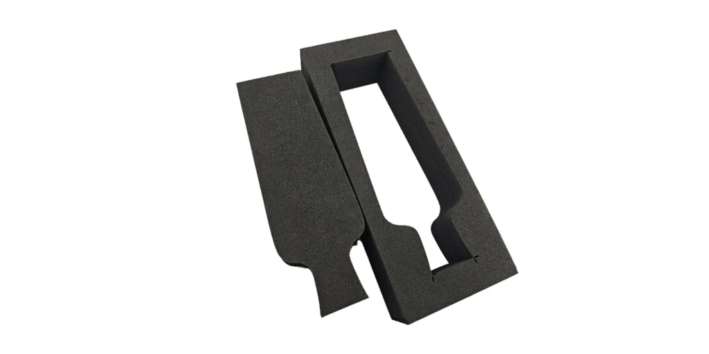 displays two black foam packaging inserts designed to protect a rectangular item (such as a device or tool) during transport. One insert features a custom-cut rectangular cavity with notched details, while the other has a matching solid foam piece that fits perfectly into the cavity. Both inserts have a smooth, matte black finish and are presented against a plain white background, highlighting their tailored design for secure, shock-absorbent storage.