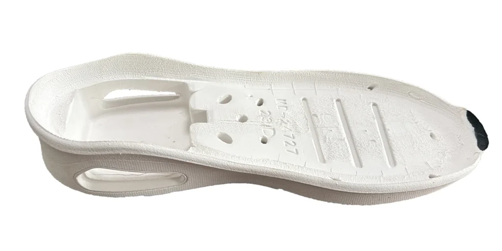 a white shoe sole. The sole has a textured exterior and is designed with multiple holes and engraved markings. It appears to be made of a lightweight material, likely intended for use in casual or athletic footwear to provide comfort and functionality.