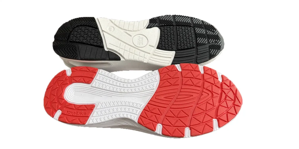 two shoe soles placed one above the other. The upper sole has a black and white color scheme, with an intricate pattern and the text "BODY FOCUS" prominently displayed in the center. The lower sole features a red and white design, also with a detailed pattern, and the text "energetics" can be seen on it. Both soles appear to be designed for traction and functionality, likely for athletic or casual footwear.