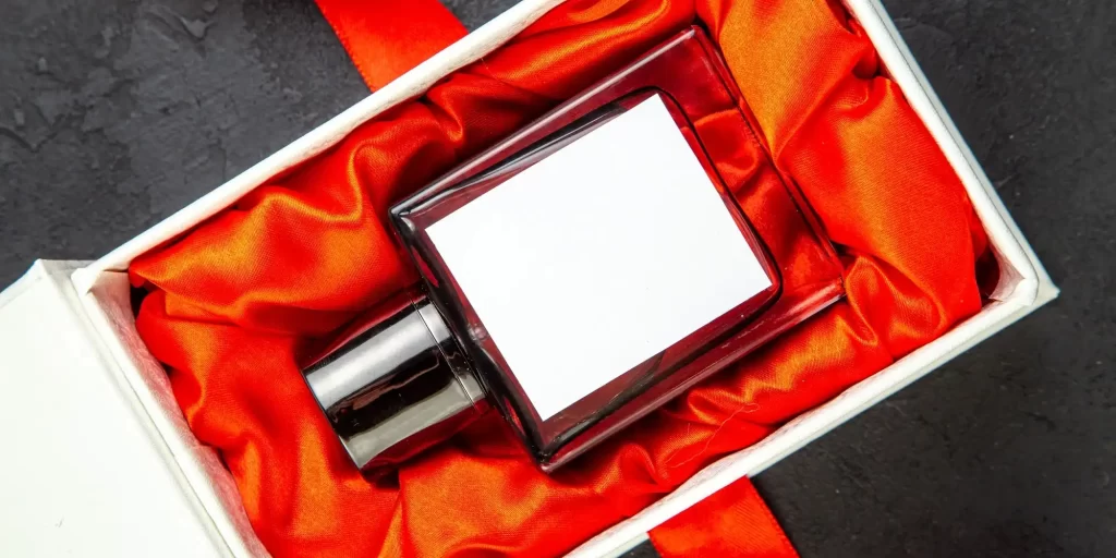 A red gift box with a black object inside the box that looks like a small square box or container. This small box is placed on a white background that contrasts with the red gift box.