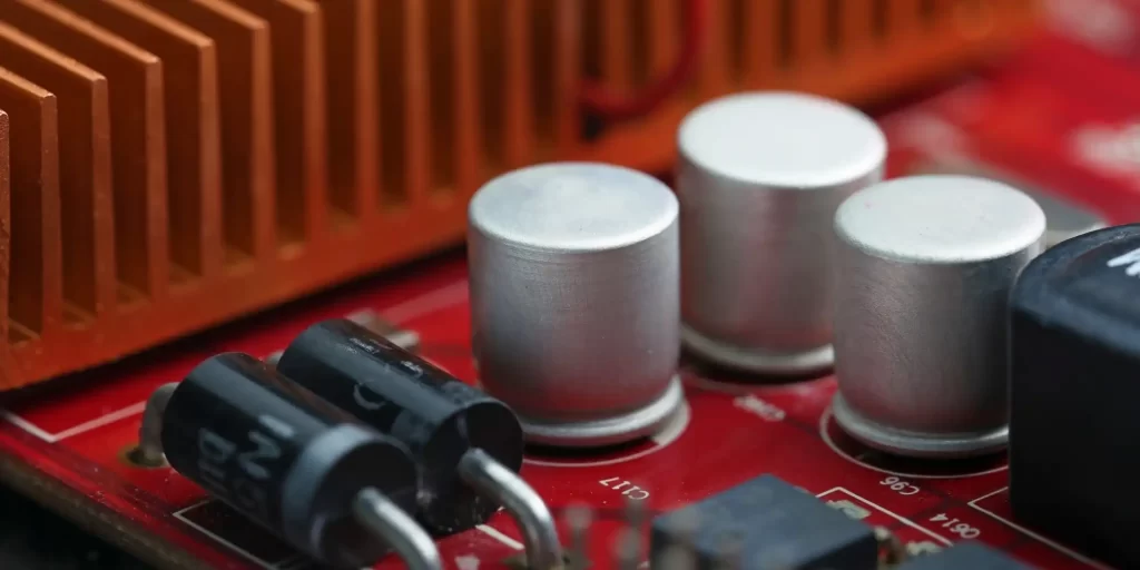 Electronic components, such as resistors, capacitors and inductors, are arranged on a circuit board. They are placed on a red surface surrounded by other electronic devices. These components include a microprocessor, a memory module, and several sensors and controllers. They are all made of metal and are held together tightly.