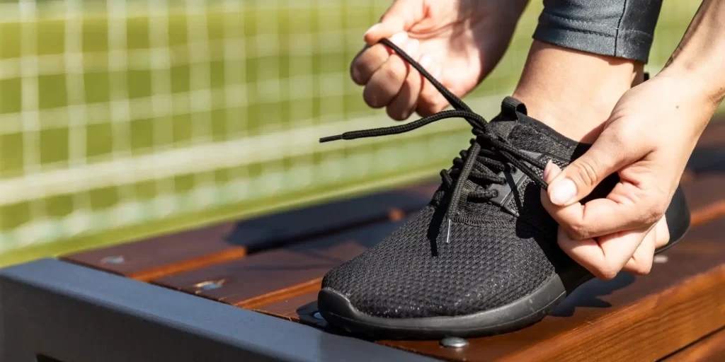 A black sneaker rested on the board and one foot was wearing the shoe and was tying the laces on it.