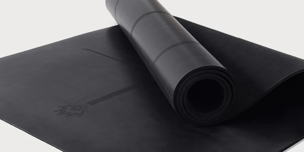 a black yoga mat. Specifically, the yoga mat is placed on a white background, with its upper part rolled up to reveal a flower pattern inside. The rest of the surface is smooth and unmarked.