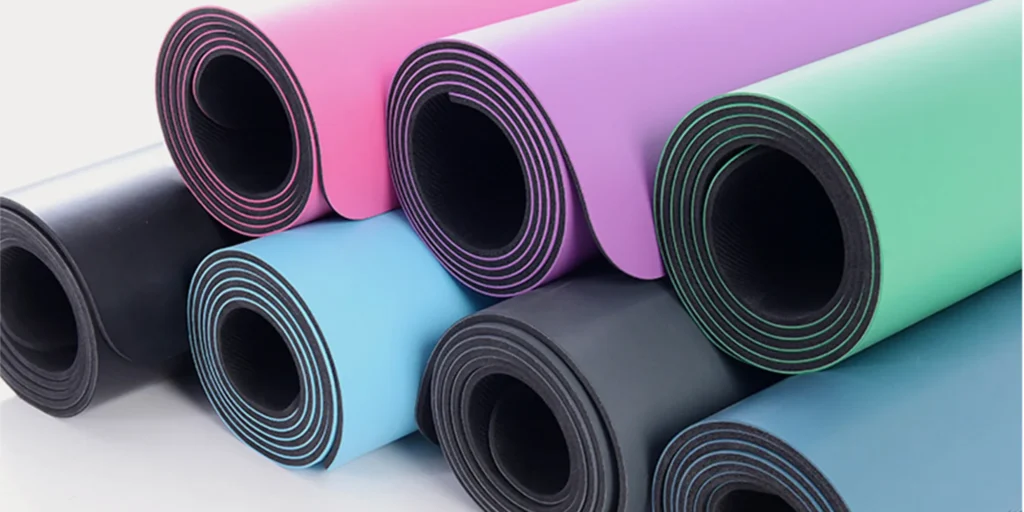 seven rolls of different colored yoga mats. From left to right, the colors are black, light blue, gray, pink, purple, green and dark blue. The surface of each yoga mat is smooth and glossy, with a circular hole in the center. These yoga mats are neatly arranged on a white background. The seven yoga mats presented in this image are not only beautiful in color but also functional. They can provide a comfortable and stable practice environment for yoga enthusiasts. Whether you’re a beginner or an experienced practitioner, these yoga mats will help you achieve your fitness goals while adding a splash of color to your workout routine.