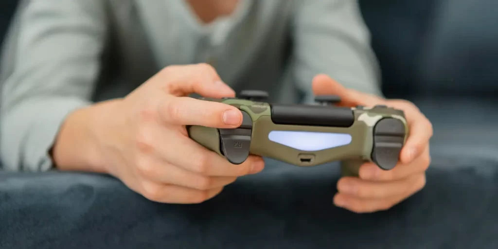 A man is holding a gamepad and is playing a PS4.