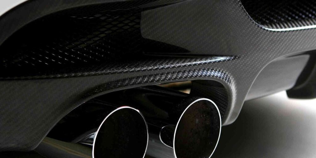 Black car exhaust pipe made of carbon fiber. It has a unique and sophisticated shape that shows modernity and elegance. It has stunning details and textures against a black background. It is part of a high performance sports car or super car with a unique look and performance.