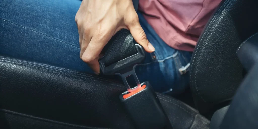 A seat, buckled in. She was dressed in a pink shirt and jeans, cell phone in hand, looking intently at the screen. The person sitting in the seat seemed to be immersed in some kind of state. As if they were thinking about something important or were enjoying their time.