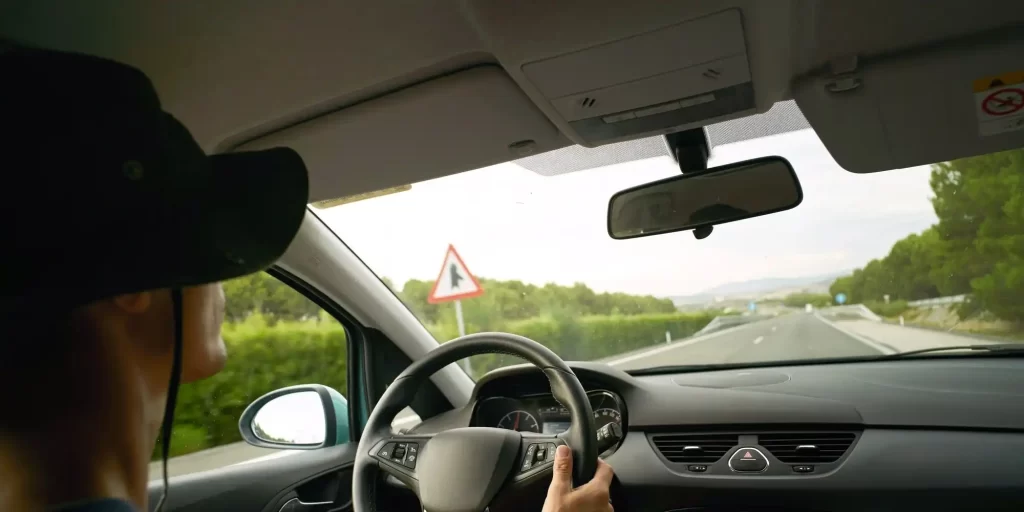 The man driving the car is wearing a black hat and sunglasses. He sits at the wheel with his hands on the stick and his eyes on the road ahead. He seemed to be immersed in his own world, focused on the process of driving. The scenery outside the car window kept changing as if time had stood still. The man's figure moved with the vehicle, displaying a unique charm. His heart is full of passion and courage, just like this car, going forward and never stopping.