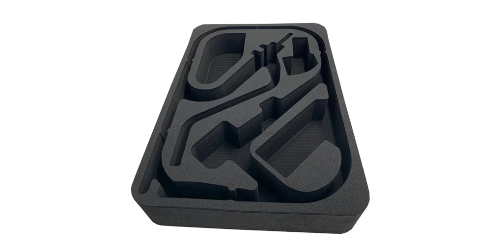 AlternativeText: A black foam insert with custom - cut compartments for securing items. Caption: Custom - Cut Black Foam Insert for Protective Packaging Description: This image features a black foam insert designed with precisely cut compartments. Each compartment is shaped to securely hold specific items, providing protection during storage or transport. The foam insert has a structured, tailored design, ensuring that objects fit snugly. The background is plain white, which highlights the details and contours of the foam’s cut - out sections, emphasizing its purpose - built nature for safeguarding delicate or valuable items.
