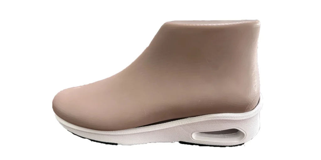 a shoe has a smooth, beige upper part that extends to form a sort of ankle - high design. The sole is white and features a noticeable cutout detail on the side. The overall appearance suggests a modern and sleek design, potentially combining style and functionality in footwear.