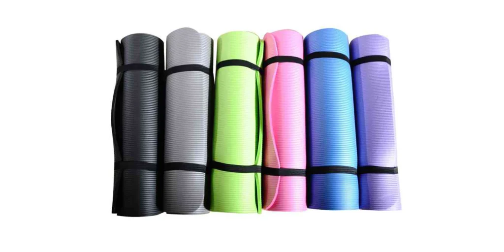 A row of yoga mats in black, gray, green, pink, blue and purple colors are neatly arranged against a pure white background. Each mat is tied with a black strap to keep it rolled up and portable. The vibrant colors make them stand out from the rest.