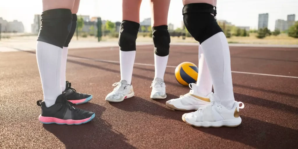 On the volleyball court, three girls stand in front of the ball wearing sneakers and socks. They seem to be enjoying the game or preparing to attack, defend or serve. One young girl is holding a basketball and the other is holding a volleyball. They all look relaxed and seem to be immersed in the fun of the game.