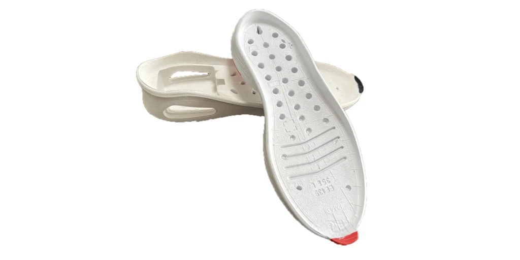 two white shoe soles. One sole is designed with numerous holes and some engraved markings, along with a red toe tip. The other sole has distinct cutout sections. Both soles appear to be made of a lightweight material, likely intended for use in footwear to provide comfort and specific functional features.