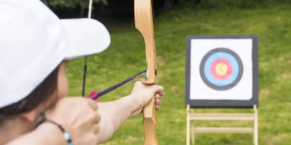 The woman held her bow and arrow, aiming at her target. Her eyes are firm and focused, as if she is preparing for an important match or performance. There is a number on the target that represents her archery score. She is wearing a white T-shirt and a black cap and holding a bow and arrow, showing confidence and courage.