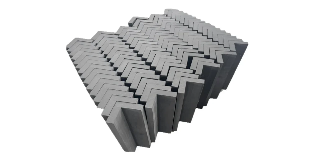 shows a collection of gray, L-shaped blocks assembled into a cohesive 3D structure with a distinct herringbone (zig-zag) pattern. The blocks interlock neatly to create a textured, geometric surface, and the entire arrangement is presented against a clean white background. The design suggests it could be a decorative element, a modular building component, or a functional industrial part, emphasizing its structured, repeating form.