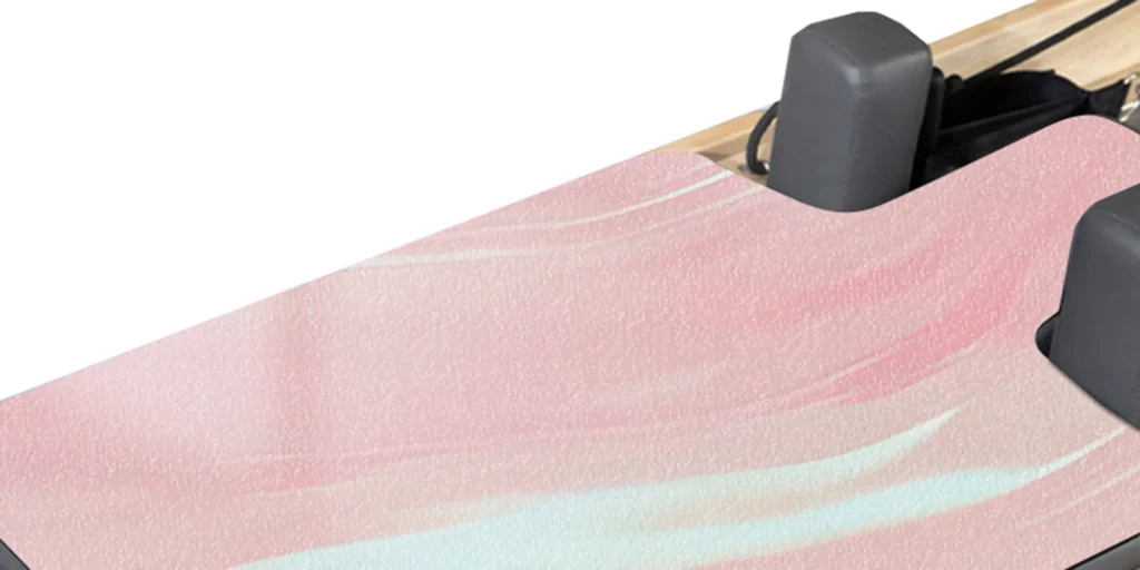 a close-up view of a piece of pink marble. The surface of the marble displays a variety of textures and patterns, including swirling streaks of white, light blue, and other shades intermingled with the primary pink hue. On either side of the marble are two black rectangular blocks, which appear to be part of some sort of equipment or furniture. The background is predominantly white, providing a stark contrast to the vibrant colors of the marble. Overall, the image highlights the natural beauty and intricate details of the marble's texture.