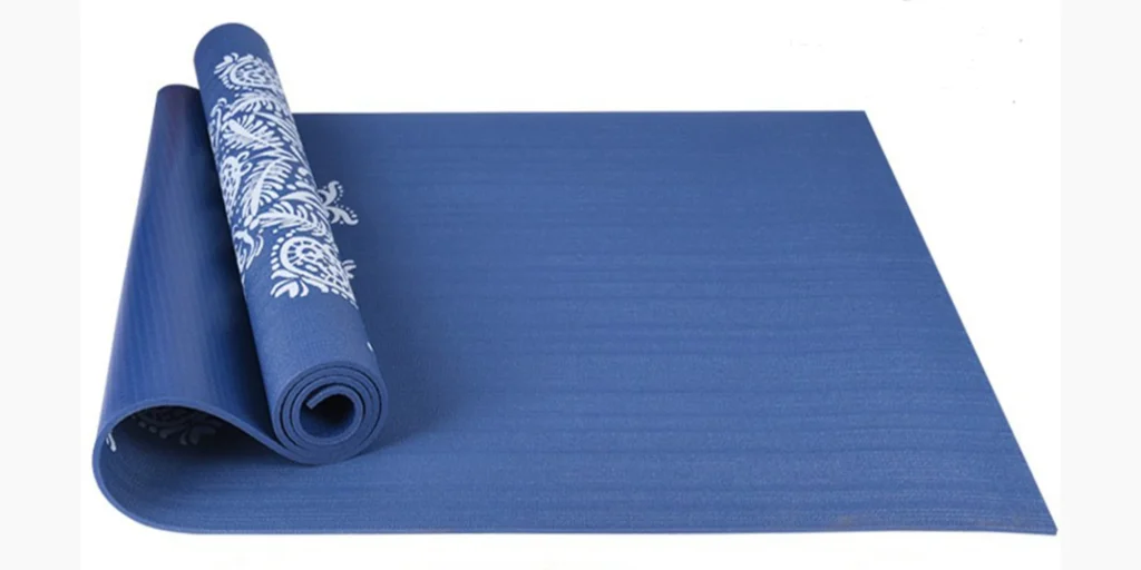 a rolled yoga mat placed on a flat surface. The mat is primarily dark blue with a decorative pattern on one end. This pattern features intricate white designs, giving it an elegant appearance. The mat appears to be made from a soft material suitable for practicing yoga or other fitness exercises. The background is plain white, highlighting the mat and its design.