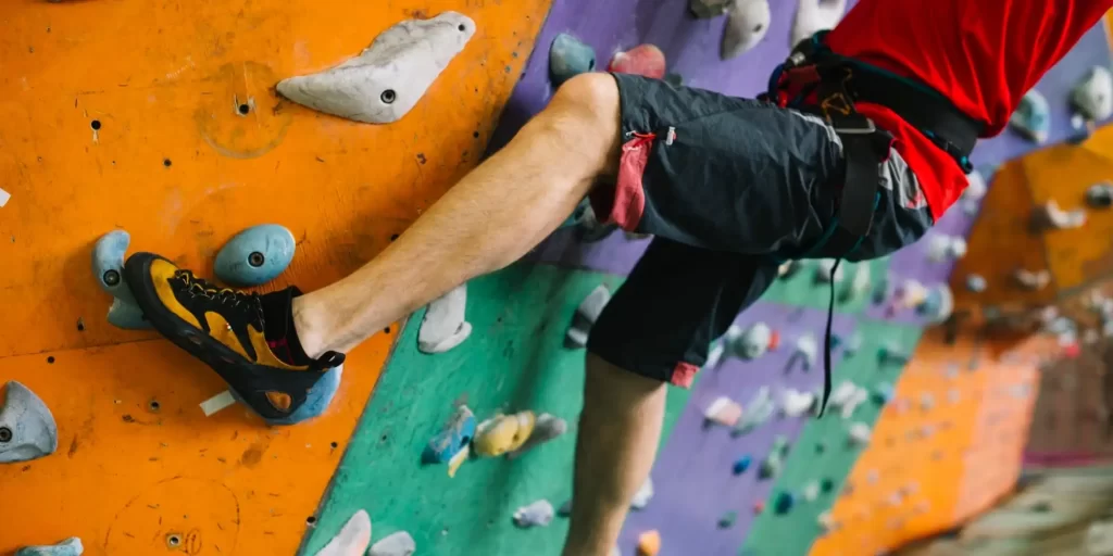 A rock wall is the most intimate contact between a male climber and the rock. He stands in front of the rock wall, hands grasping the bars and handrails, ready to climb. His feet move across the ground and his body leans upward as he works his way to greater heights. The wall's colorful climbing slabs, the rock, and the climber's body make a beautiful picture.
