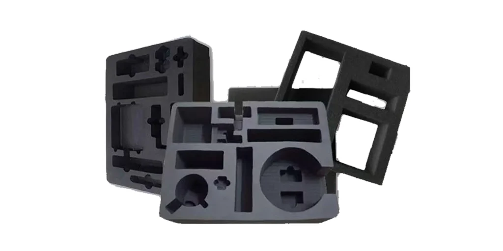 displays a stack of custom foam inserts in black and gray, each with unique, precision-cut cavities tailored to specific tools, electronics, or components. The designs include circular, rectangular, and specialized cutouts, along with a frame-style foam piece, all designed to securely hold items during transport or storage. The contrasting colors and varied shapes highlight their functional, custom-fit construction for protection and organization.