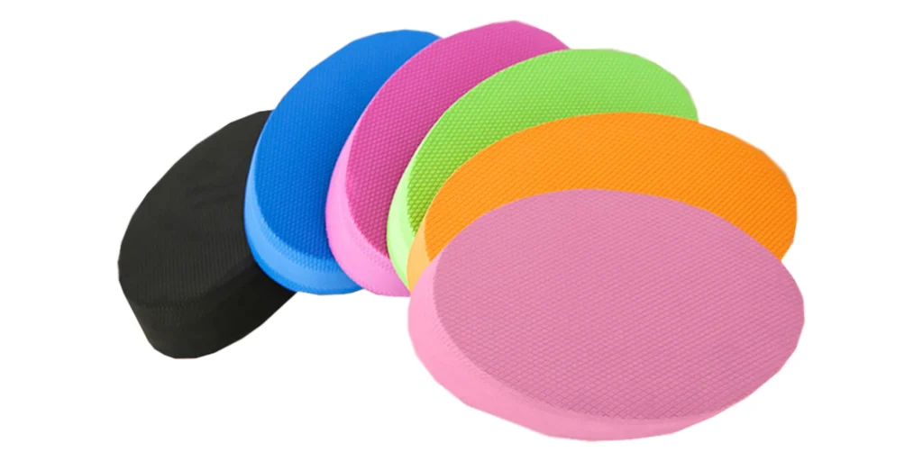 seven colorful foam pads arranged in a fan-like formation. Starting from the bottom left corner and moving clockwise, the colors of the pads are black, blue, pink, green, orange, and another pink pad. Each pad has a textured surface, likely designed for grip or cushioning. The arrangement creates a visually appealing array of colors, suggesting a playful and creative atmosphere. The background is plain white, which contrasts with the vivid colors of the foam pads, making them stand out more prominently.
