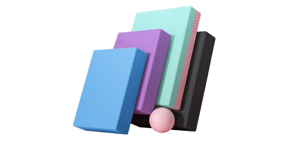 five colorful foam mats arranged in a stack against a white background. Starting from the bottom to the top, the mats are colored in a gradient sequence: dark black, light purple, bright blue, sunny yellow, and ending with a warm orange. Each mat has a textured surface, suggesting their use for safety and comfort during physical activities such as gymnastics or exercise. The precise arrangement and the variety of colors create a visually appealing contrast with the white background, highlighting the functional versatility of these foam mats.