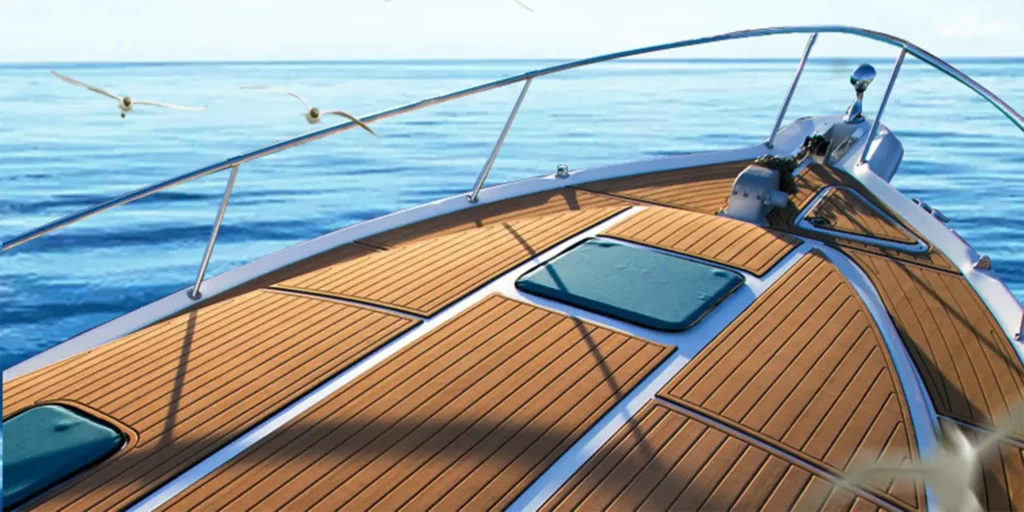 the bow of a luxurious yacht sailing on calm blue waters. The deck is made of polished wood, giving it an elegant and warm appearance. There are two teal-colored cushions placed in front of the helm station, suggesting a comfortable seating area for relaxation or navigation. In the background, we can see the vast expanse of water stretching to the horizon under a clear sky. A few seagulls are flying overhead, adding life to the serene maritime scene. The overall atmosphere conveys tranquility and leisure associated with yachting.