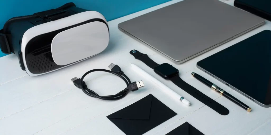 Pictured are a white and black VR glasses, a laptop, a pen, a black Apple Watch, and a white data cable.