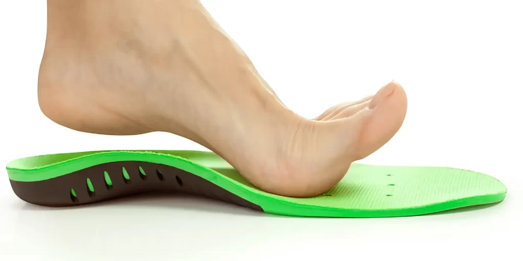 a female leg positioned above an orthopedic insole. The insole is green, which might indicate a specific type of support or design feature, and it's common for orthopedic insoles to come in various colors to denote different arch supports or cushioning levels. These insoles are often used to correct foot alignment, provide additional support, and relieve discomfort caused by various foot conditions or to enhance comfort for everyday wear.