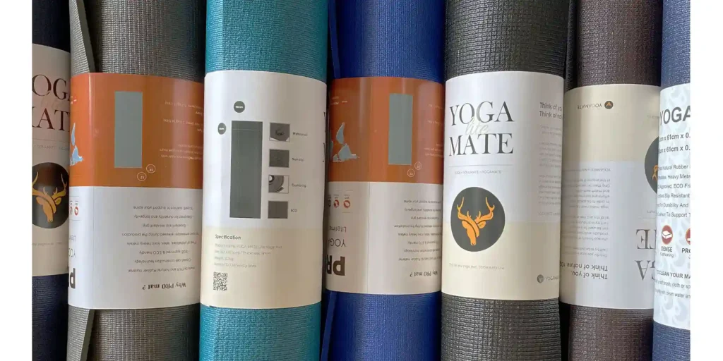 a variety of yoga mats with different colors and patterns. They are neatly arranged in rows, each with its own label showing the color, size, material and other information. For example, there is a blue one in the middle of the picture, which has “YOGA MATE” written on it. There’s also a black one on the far right that says “YOGA”.